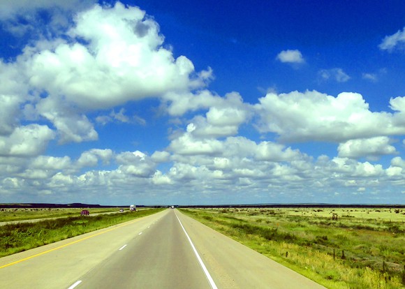 Open-road highway in North Dakota under a blue sky with white puffy clouds