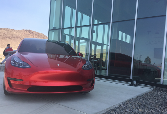 A red Model 3 prototype next to a glass building