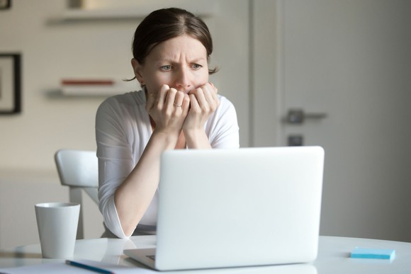 A worried looking woman looking at her laptop computer at work.