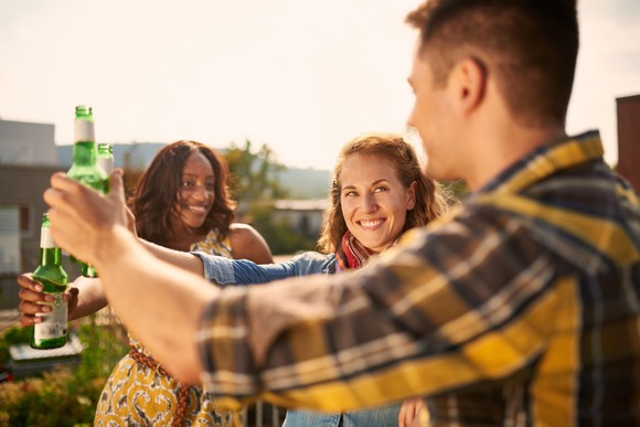 Three young adults outside toasting a beer.
