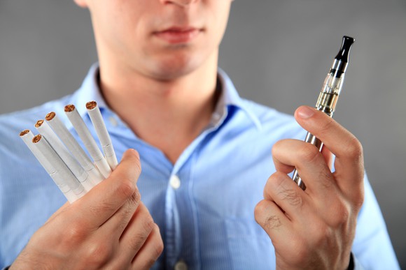 A young man deciding between cigarettes and an electronic cigarette.