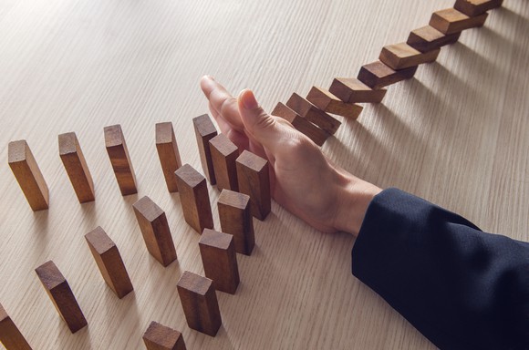 Hand preventing wooden blocks from falling and causing a cascading chain reaction