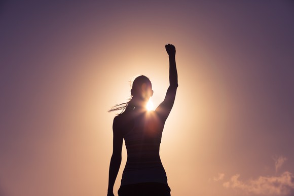 Woman raising her fist in silhouette against a golden sunrise.