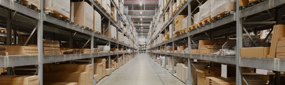Aisle of an industrial warehouse with pallets on metal shelves going all the way to the ceiling