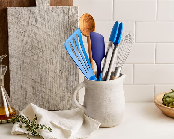Spatulas, a whisk, and a wooden spoon, in a jar sitting on a counter.