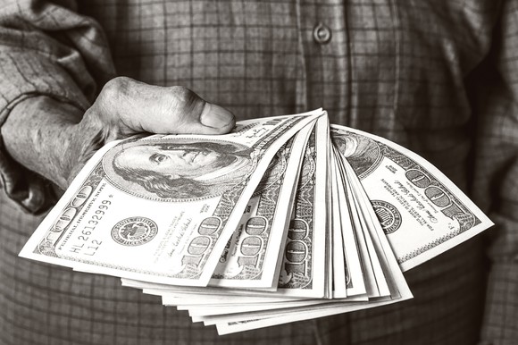 The hand of an elderly man holding a dozen $100 bills.