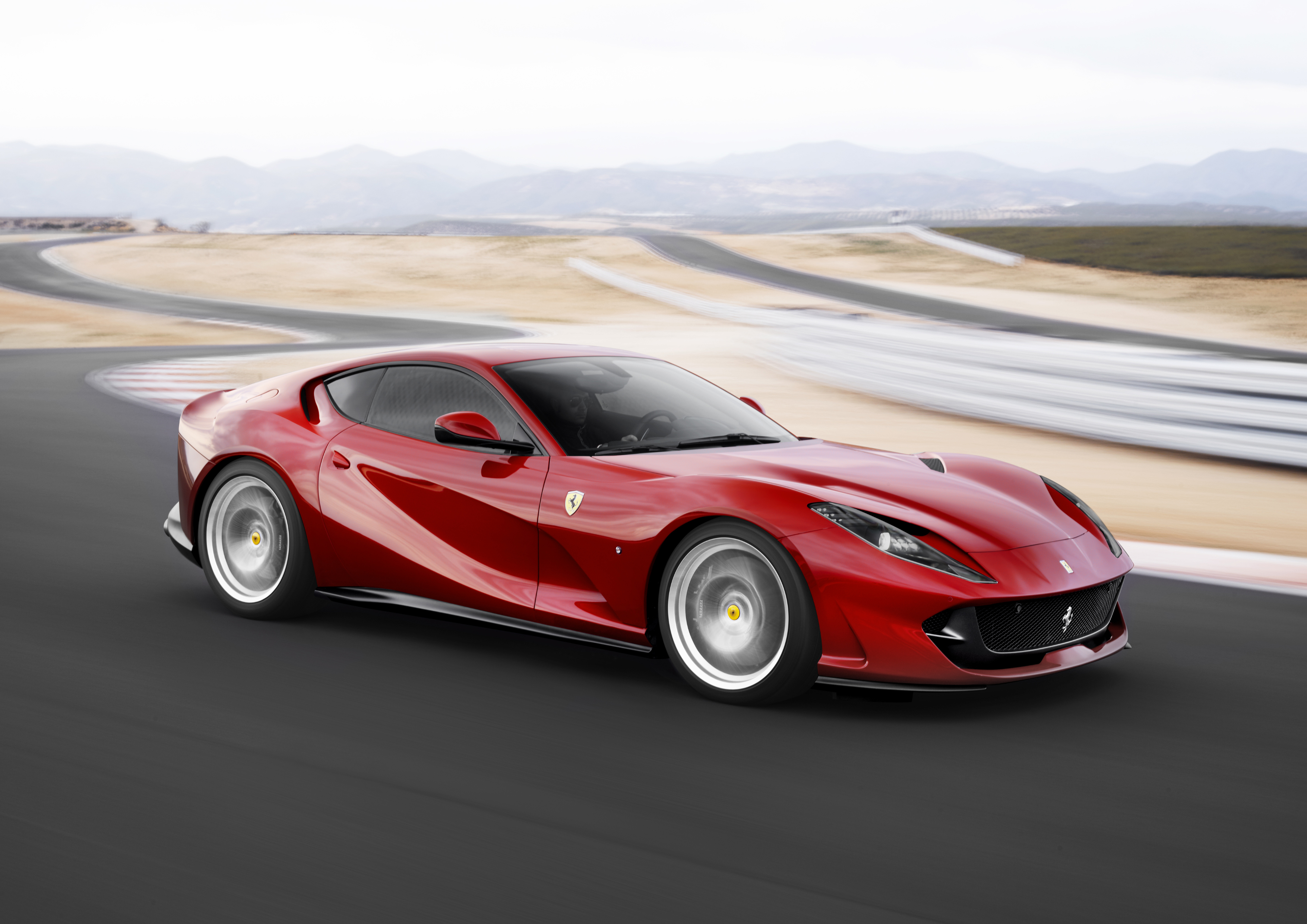 A red Ferrari 812 Superfast sports car at speed on a winding road.