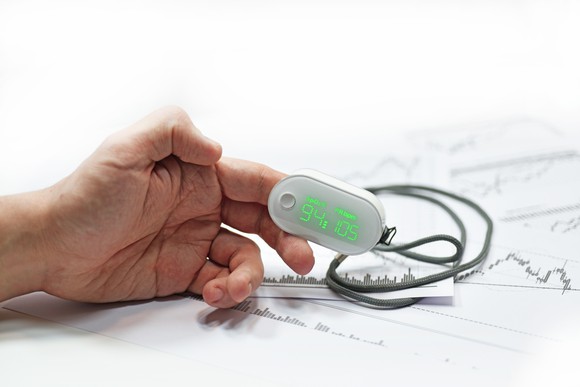 Hand resting on top of papers with index finger in pulse oximeter