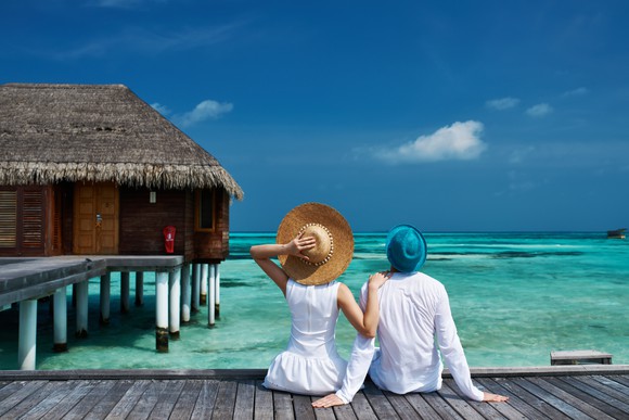 A couple sits on a dock looking out into a clear blue sea.