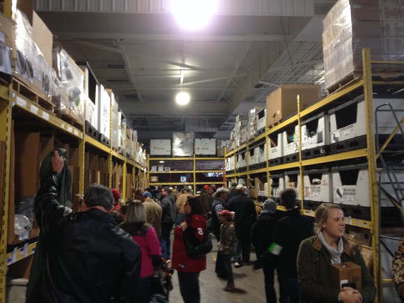 Liquidity Services location, with warehouse-style shelves going to the ceiling and dozens of shoppers in the aisle.