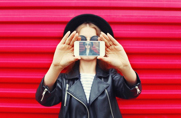 Fashionably dressed woman takes selfie with smartphone.