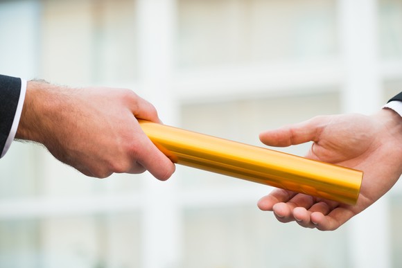 A businessperson passing a gold baton to another businessperson