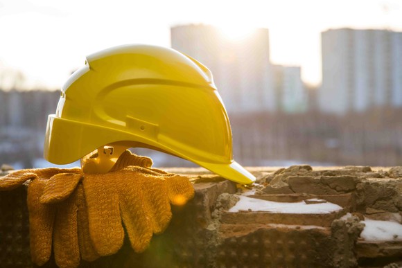 A yellow hard hat sitting on top of gloves on a ledge.