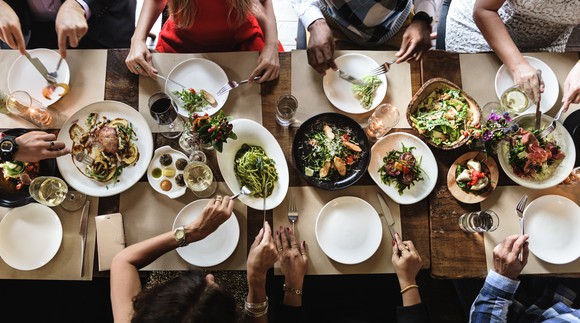 Eight people sitting at a long, skinny table eating dinner.