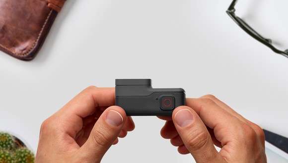 View from above of two hands holding a GoPro HERO5 camera, with a wallet and glasses on a table below