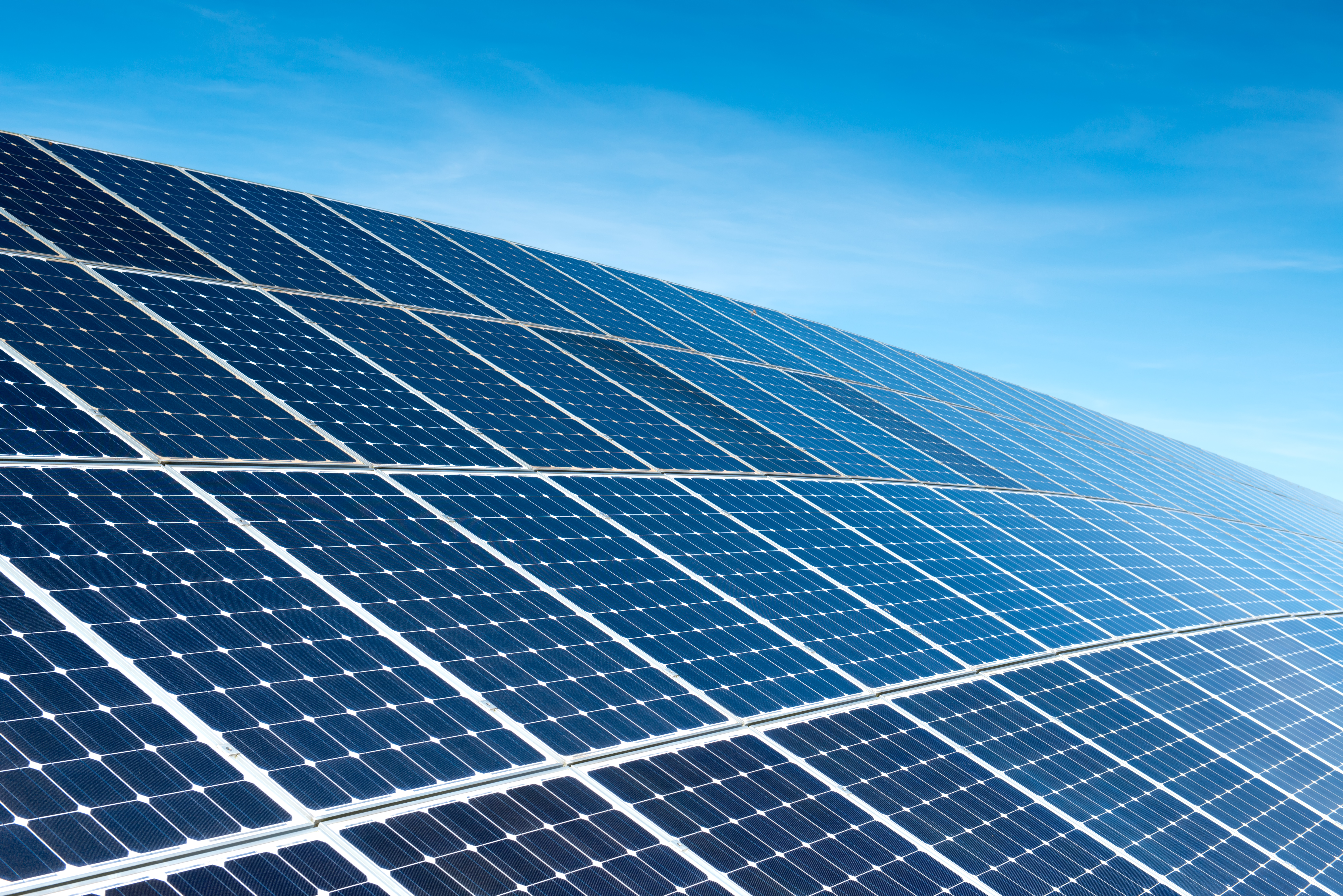 Solar panels mounted on a flat surface in a row with a sunny sky in the background.