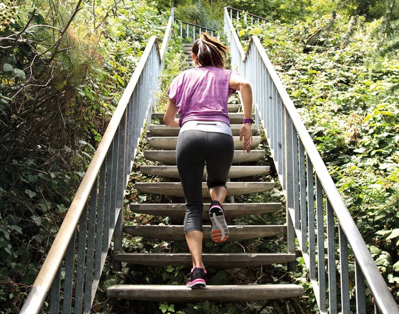 Woman in workout gear running up stairs with a Fitbit bracelet.