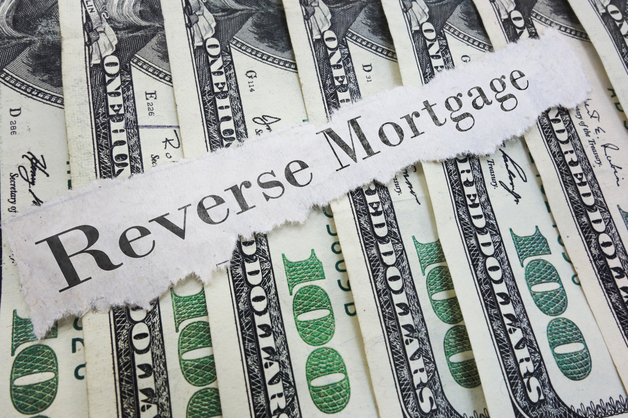 The words "reverse mortgage" on a torn piece of paper, on top of hundred dollar bills