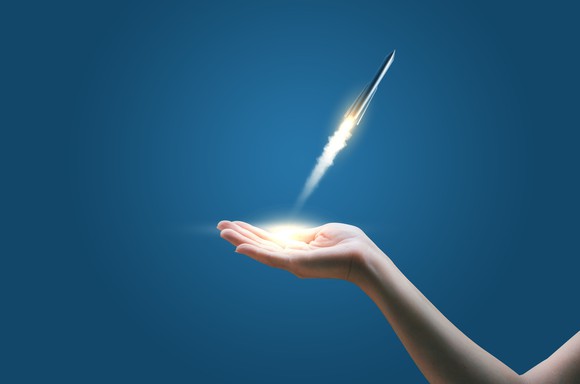 A miniature rocket taking off from a person's open hand.