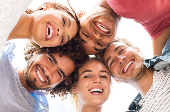 Five smiling men and women with their heads together in a circle.