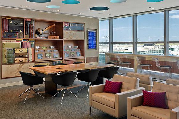 An airport lounge with leather chairs and a long wood table.