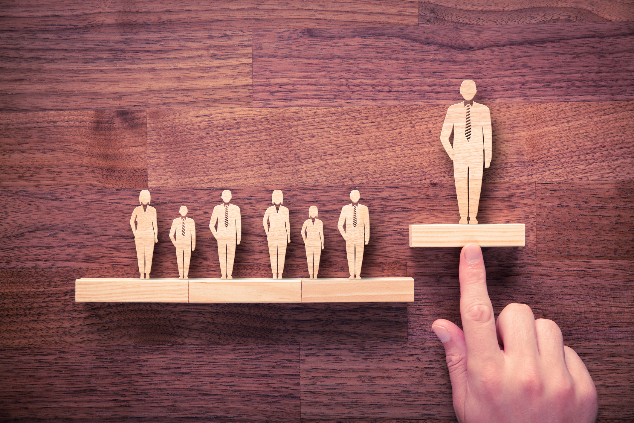 Wooden figures of people with one pushed higher than the others