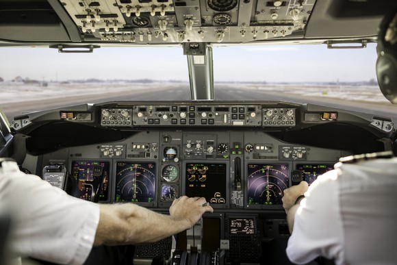 A pilot pulls back the throttle in a cockpit.