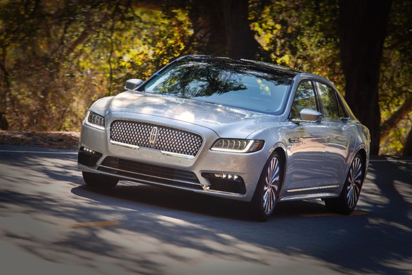 A silver Lincoln 2017 Continental driving on a road against a backdrop of autumn-leaved trees.