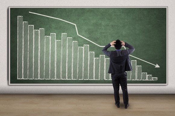 An arrow showing the downward trend of a chart on chalkboard with a business man in front of it.
