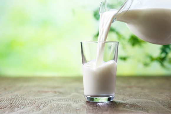 Milk is being poured into a glass outdoors.