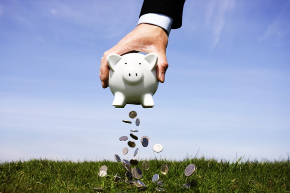 Hand shaking money out of a piggy bank.