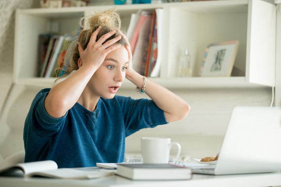 A woman holding her head with her hands and staring in disbelief at her laptop