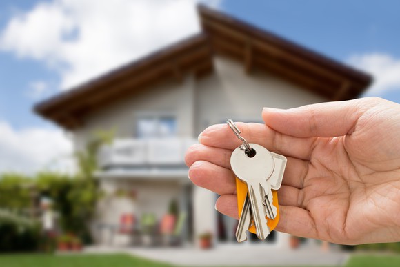 Hand holding house keys with a home in the background