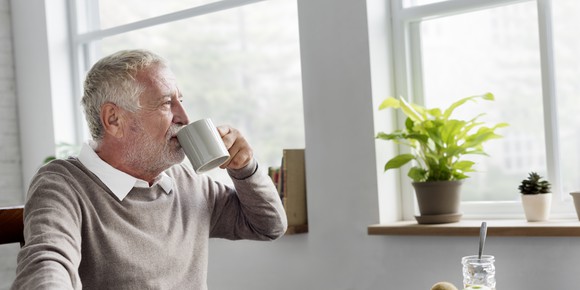 A senior man drinking coffee and looking out the window.