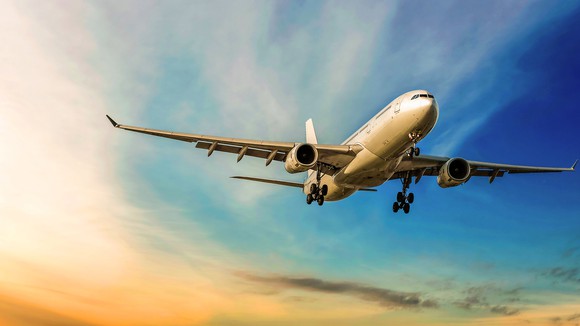 A Boeing 787 Dreamliner airplane in flight with clouds in sky in background.