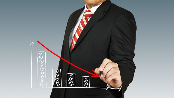 Man dressed in suit drawing red arrow trending down over bar chart