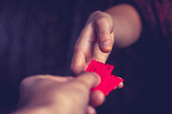 A hand giving two red tickets to another hand