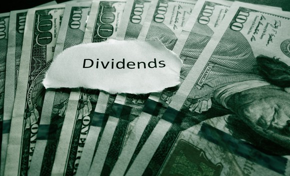 Photo of paper cutout with word "dividends" on top of $100 bills