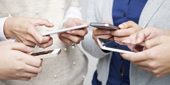 Four people huddled around their smartphones.