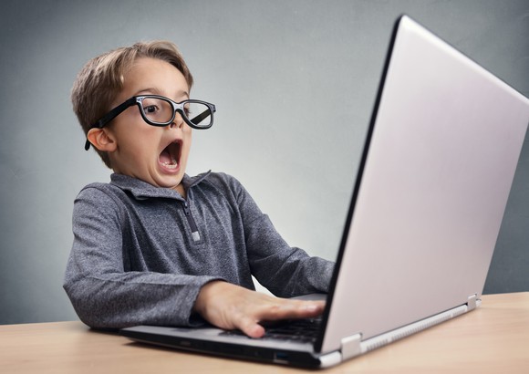 Young boy in big glasses sitting at laptop and amazed, mouth wide open