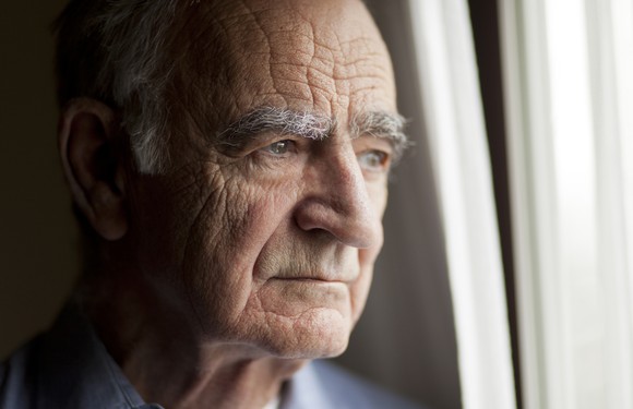 A senior man staring out a window.