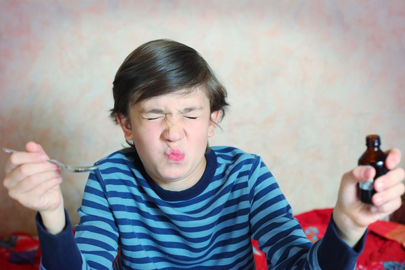 Boy grimacing after swallowing a spoonful of medicine.