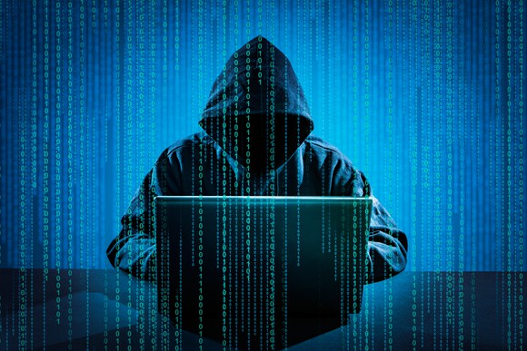 A person wearing a hood covering his or her face sitting in front of a computer