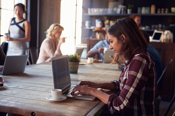 girl working at laptop in coffeeshop, others there also on laptops
