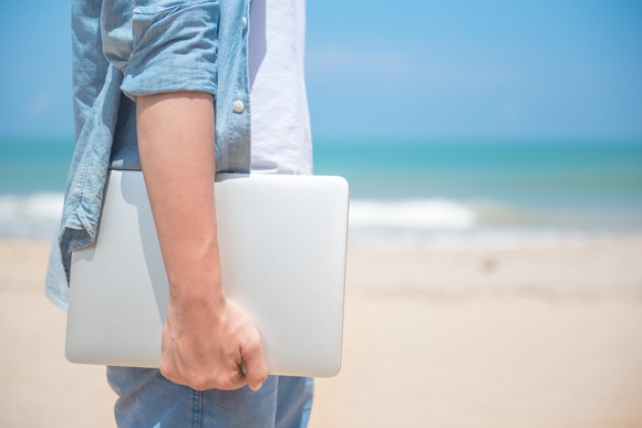 Man hand holding laptop at the beach