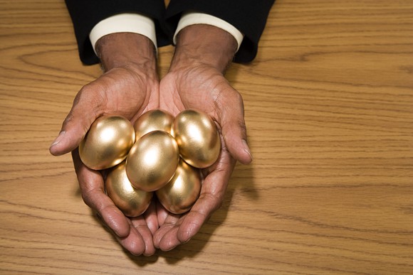 Man's hands resting on a wood table holding several golden eggs