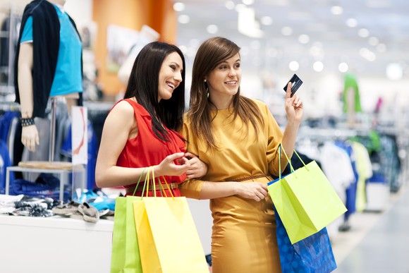 Two women shopping in a department store, one holding a credit card.