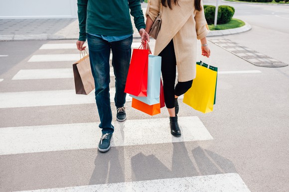 Two people on a crosswalk, holding shopping bags.