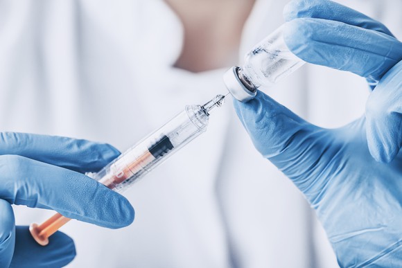 Two gloved hands holding syringe and vial 