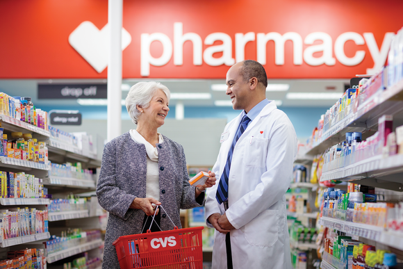 CVS pharmacist in white lab coat assists elderly female customer in store aisle.